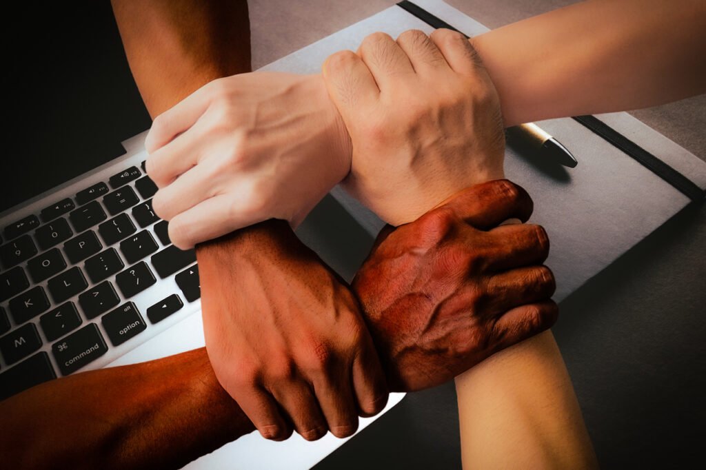 Diverse hands united over a laptop, symbolizing teamwork and collaboration among different races.